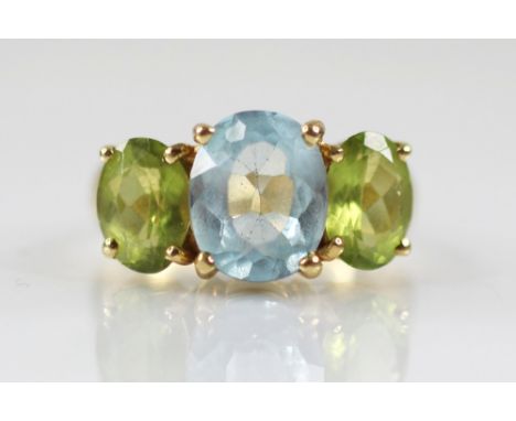 A topaz and peridot cocktail ring, the central oval blue topaz measuring 10mm x 8mm, with an oval peridot to each side, claw 