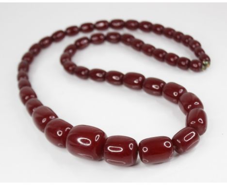 A cherry amber bead necklace, comprising forty-nine barrel shaped beads, measuring between 11mm x 9mm and 26mm x 24mm, spring