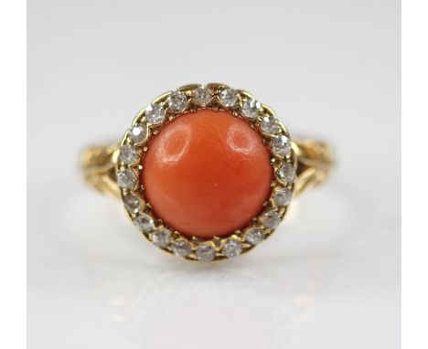 A Victorian coral and diamond 18ct gold ring, the central coral cabochon measuring 9.5mm diameter, within a border surround o