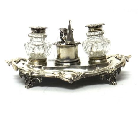 A Victorian silver twin bottle inkstand, of shaped oval form, decorated with a scrolling border, raised on four scrolling fee