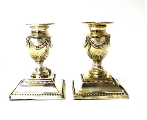 A pair of Victorian silver candlesticks, each of urn shaped form, with pendant swag decoration, on beaded square bases and wi