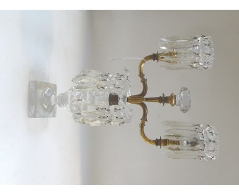 A Victorian gilt metal mounted cut glass two branch candelabra, hung with cut glass drops over an urn shaped body and square 