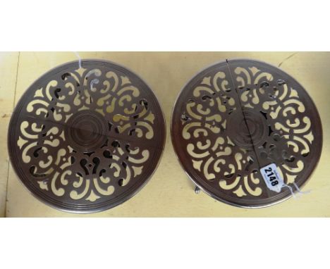 A pair of expanding table trivets, early 20th century, each circular white metal pierced plate on turned supports and castors