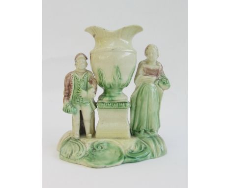 A Staffordshire creamware group, modelled as a man and woman standing either side of an urn shaped vase supported on a plinth