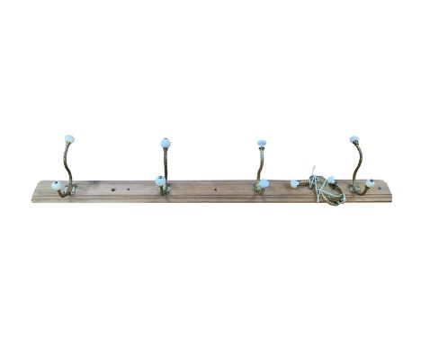 A set of five brass and ceramic coat hooks, mounted on a moulded pine support, width 102cm.