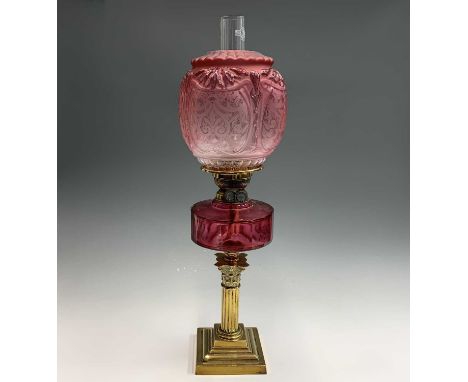 A late Victorian cranberry glass and brass oil lamp, raised on Corinthian column base and with etched and moulded cranberry g