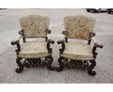 A pair of Italian carved walnut armchairs of 17th century design with tapestry seats, backs and arm pads, on scroll stretcher
