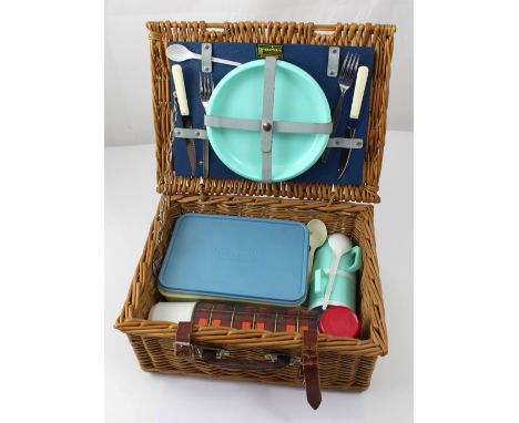 A vintage Brexton wicker picnic basket with sandwich box, cups, plates, knives and forks and a non-matching flask.