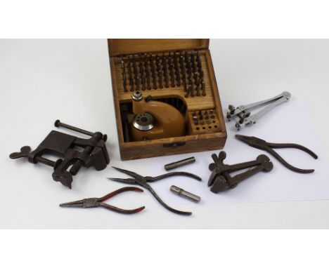 A wooden case containing a quantity of watchmakers equipment to include a watchmakers clock, vintage staking tool, press and 