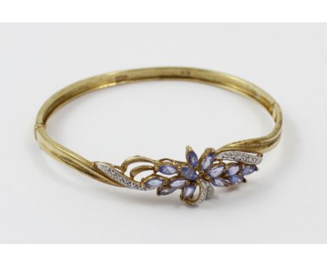 A 9ct gold bangle with central floral decoration of lilac and white stones, approx 10.1g.
