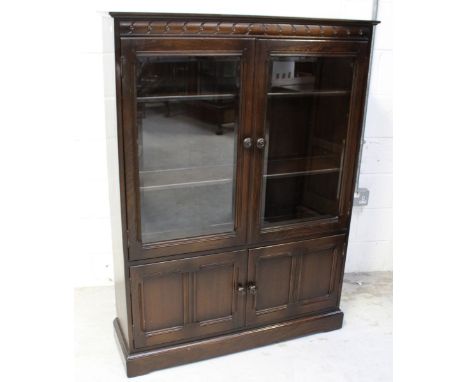 An Ercol dark stained 'Old Colonial' bookcase with twin bevel glass doors, two shelves to interior, above twin cupboard doors