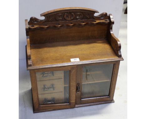 An Edwardian Arts and Crafts style oak smoker's cabinet with pipe rack gallery above twin glazed doors, which open to reveal 
