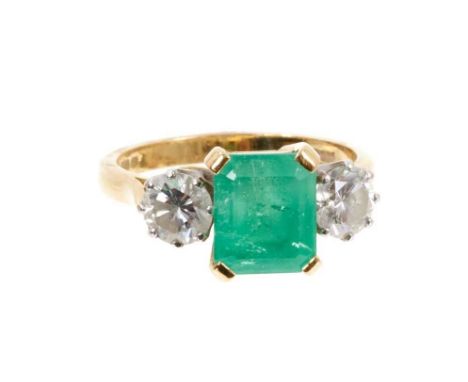 Emerald and diamond three stone ring with a rectangular step cut emerald measuring approximately 8.3mm x 7mm x 5.8mm, flanked