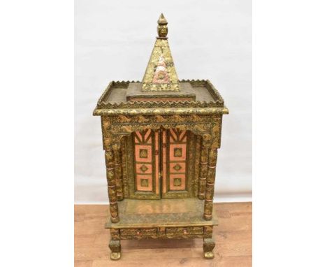 Unusual Indian embossed metal mounted temple cabinet, with finialled top and recessed cupboard doors with drawer below on bra