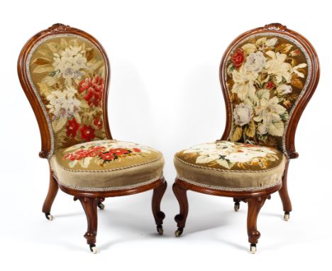 A pair of Victorian mahogany framed spoon backed lounge chairs. With carved central motif to the top rail, both upholstered i