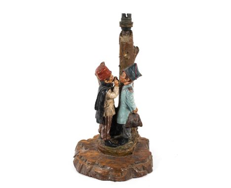 A Continental glazed terracotta lamp base, circa 1900. Modelled as two boys standing before a tree-trunk column, mounted on w