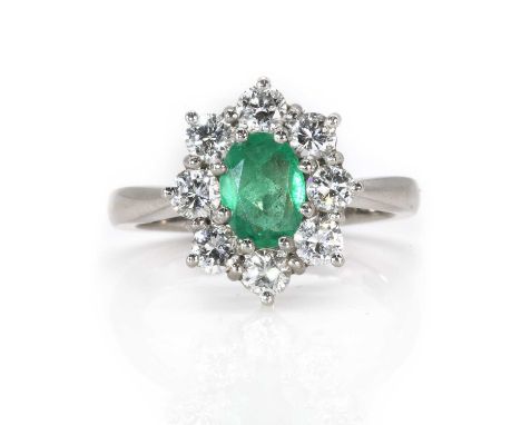 A platinum emerald and diamond cluster ring, with a central oval faceted emerald, 5.50mm x 7.50mm, surrounded by eight round 