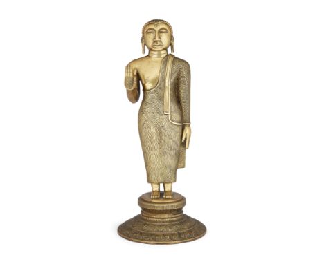 A brass figure of Buddha, Sri Lanka, 19th century, solidly cast standing on a circular lotus base, his right hand raised in a