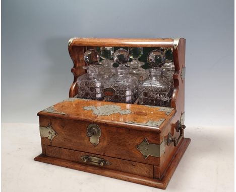 An oak Tantalus/Games Box with plated strapwork mounts with three decanters and stoppers, a hinged compartment opening to rev