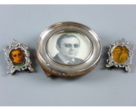 A PAIR OF SILVER FLORAL DECORATED MINIATURE EASEL PORTRAIT FRAMES, 4.5 x 2.5 cms, 0.7 ozs, London 1981 and a circular silver 