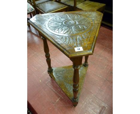 AN OAK TRIANGULAR TWO TIER SIDE TABLE, the carved and moulded edge top with canted corners and decorative frieze on block and