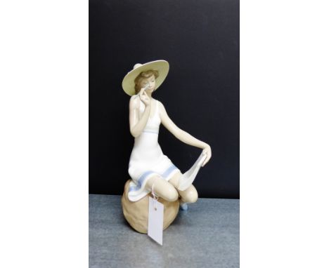 A Nao porcelain figure of a Girl modelled seated in a sun hat and writing notes, 30cm high