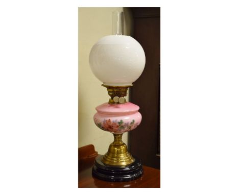 Victorian oil lamp having a pink glass reservoir with painted floral decoration, brass bell shaped pillar and standing on a b