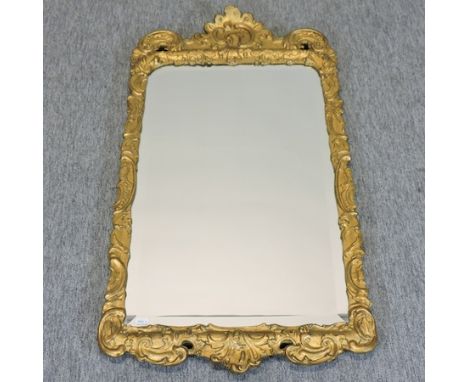 A carved and gilt framed wall mirror, the rectangular bevelled plate, with a scrolled surround, 105 x 53cm 