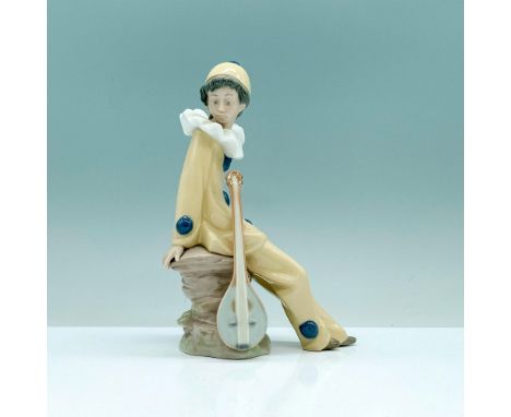 A glazed figure of a young boy in a yellow jester's outfit sitting on a rock with his instrument by his side. Nao by Lladro b