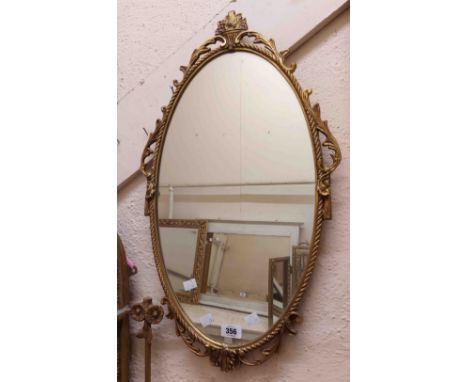 A vintage brassed cast metal framed oval wall mirror with decorative border