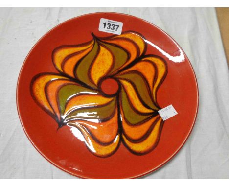 A Poole Pottery plate in the Delphis range, decorated with a central abstract design in yellow, green and orange on a red gro