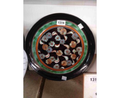 A vintage Poole Pottery charger, in the Ionian range, decorated with enamelled stylised flowerheads on a brown ground with or