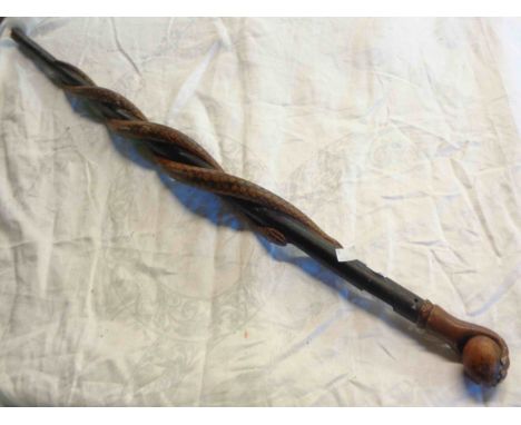 An Eastern Folk Art walking stick with finial in the form of a hand clutching an orb, two snakes coiled around the shaft of t