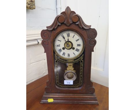 An early 20th century American walnut cased mantel clock, the scroll carved case with glass door enclosing a decorative pendu