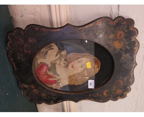 A Victorian woolwork tapestry depicting a girl with a cat, in a floral painted shaped papier mache frame, 42cm x 30cm