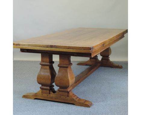 An unusually large light oak draw leaf dining table, having a plank top, on twin end supports united by a square stretcher, 4