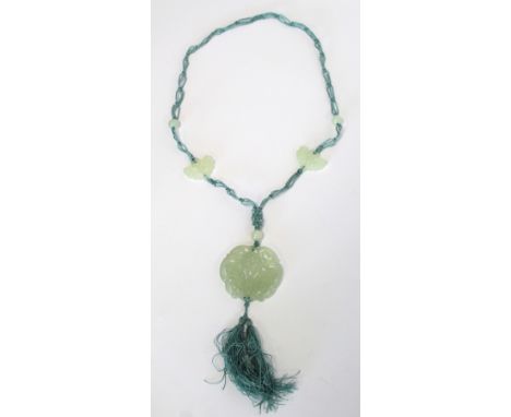 Chinese pale green jade pierced and carved roundel depicting a butterfly on a flower with pale turquoise silk tassel on woven