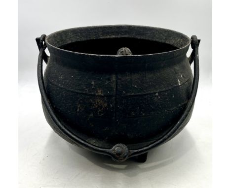 A vintage cast iron cauldron on tripod legs with tongs