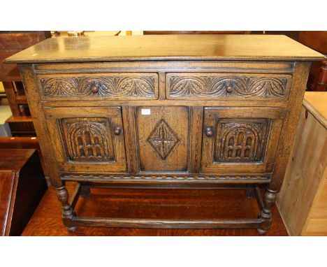 A small joined and relief carved oak dresser base having twin drawers and cupboard doors on turned and square cut supports, w