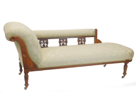 A late Victorian walnut chaise longue, upholstered in green damask fabric, the frame carved with patera, leaves, etc., on tur