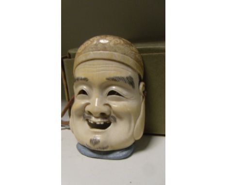 An ivory mask netsuke of Ebisu, the smiling face with black stained hair, he wears a cap brocaded with stylised clouds, 7.5cm