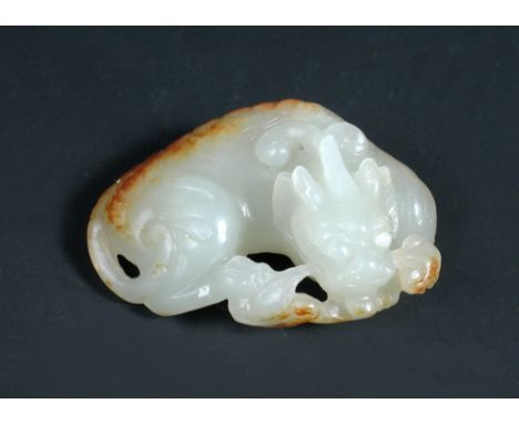 A grey mottled white jade pendant, possibly 18th century, carved as a curled dragon, lingzhih in its mouth, the nobbles of it