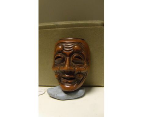 A wooden mask netsuke of a man, rosettes of hair flanking his smiling mouth and forming eyebrows above squinting eyes, 4.5cm 