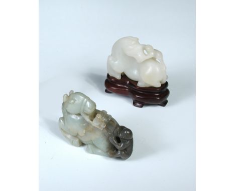 A green and grey jade group of a bridled reclining horse looking back to a fly on its back between the reins held by the grey