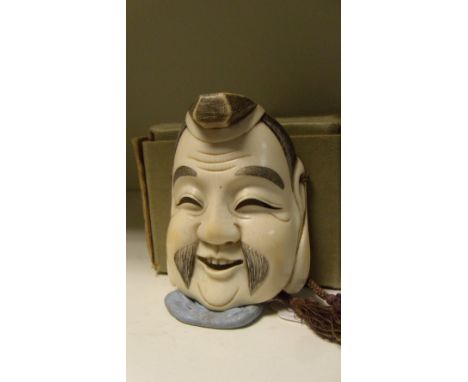 An ivory mask netsuke of Daikoku, signed Deme Tamatoshi, the smiling deity wearing a hat, his hair stained black, 7.5cm (3 in