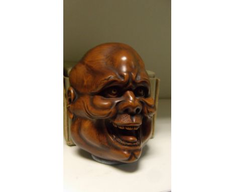 A wooden mask netsuke of a laughing bald man, signed Unpo, baggy cheeks and raised eyebrows about ivory eye whites, 9cm (3.5 