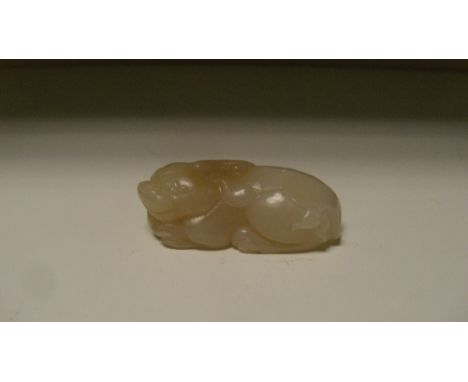 A brown mottled white jade Buddhist lion, possibly 18th century, the horned beast clasping a ball between its claws, 5cm (2 i