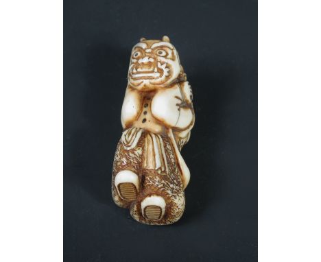 A 19th century ivory netsuke carved as a child wearing an oni's mask, his two tufts of hair and the buttons of his coat inlai