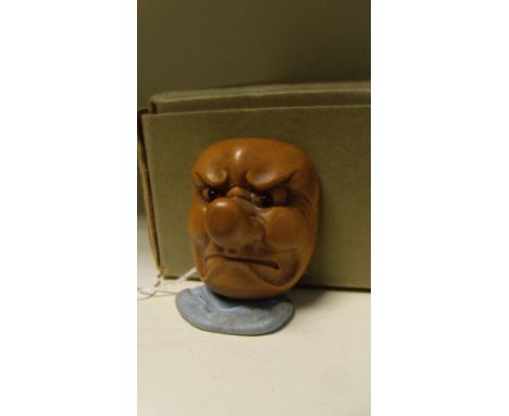 A wooden mask netsuke of a stern man with pronounced nose, his eyes inlaid in black (jet?), 5cm (2 in) high  Good