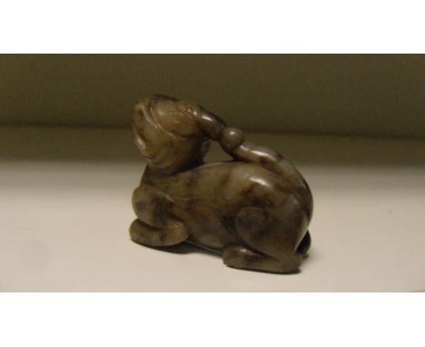 A Ming jade qilin, the tail tip of the reclining animal touching the horn on its head, one side of the beast black and the ot